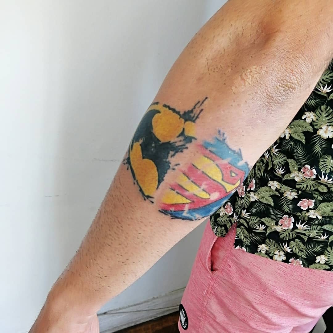 Forearm tattoo combining Batman and Superman logos
